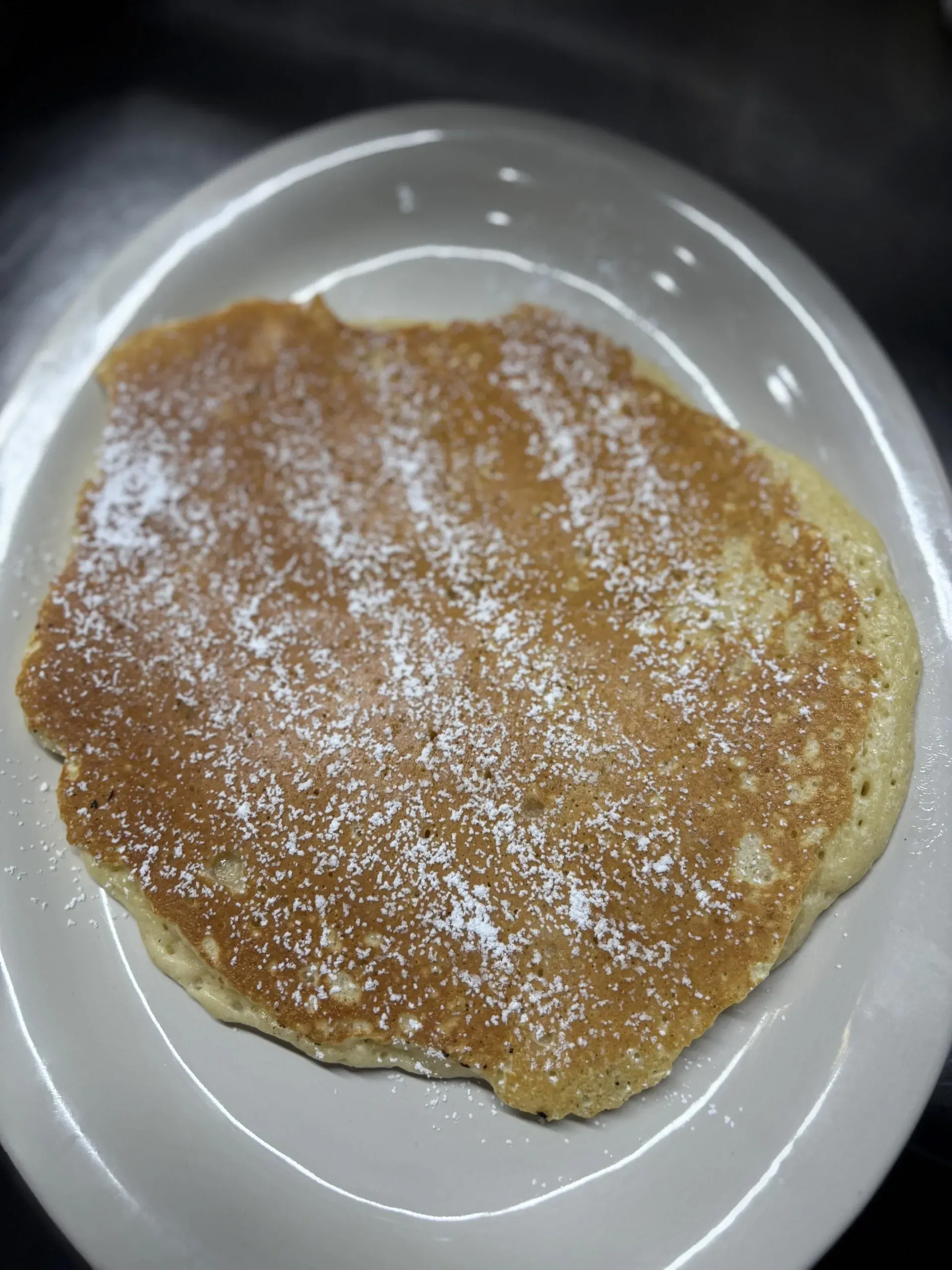 A pancake with powdered sugar on it is on a white plate