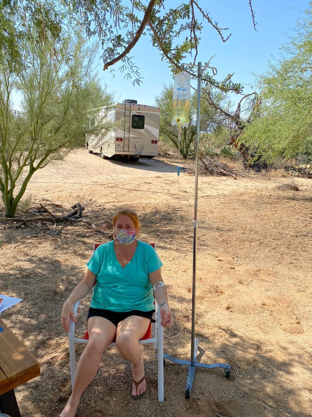 A woman wearing a mask is sitting in a chair in front of a rv.