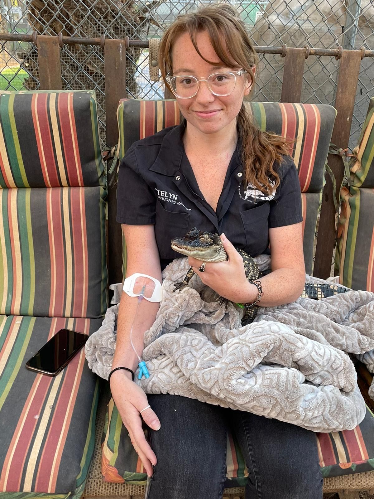 A woman is sitting on a bench holding a small alligator.
