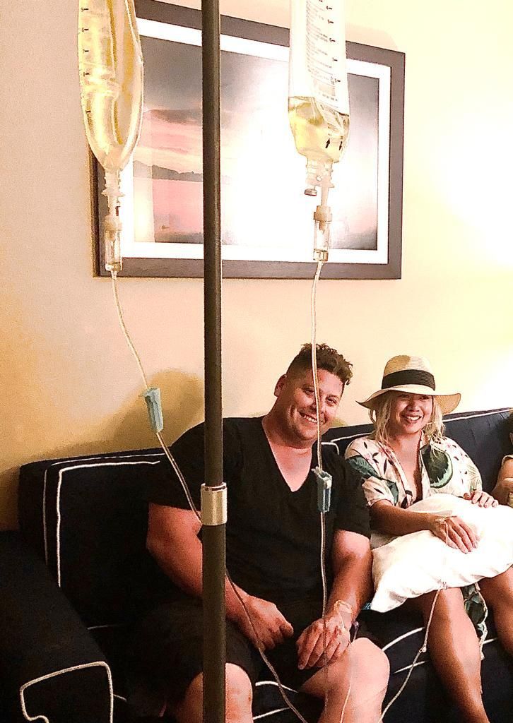 A man and a woman are sitting on a couch with an iv in their arm.