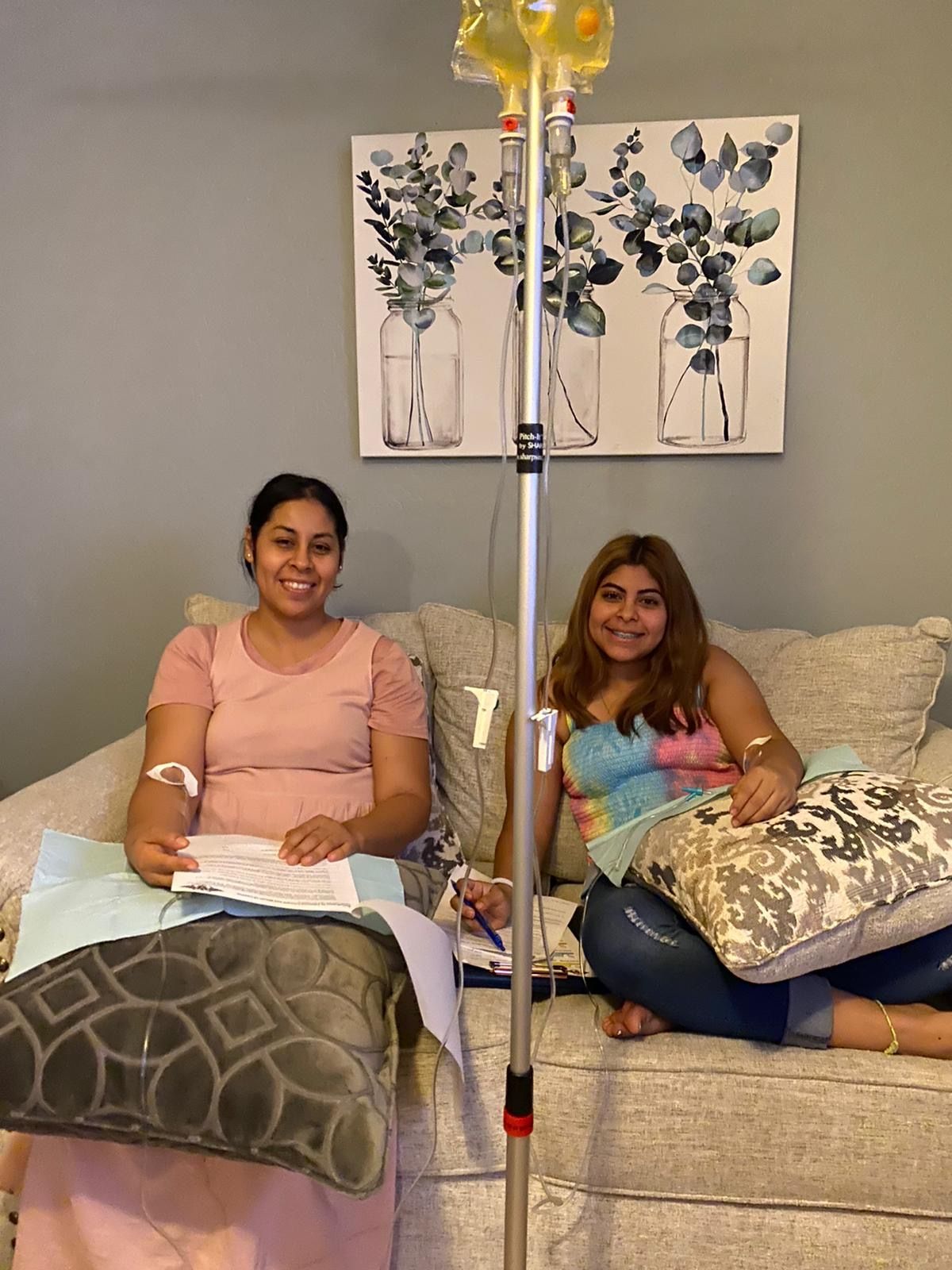 Two women are sitting on a couch with iv drips in their arms.