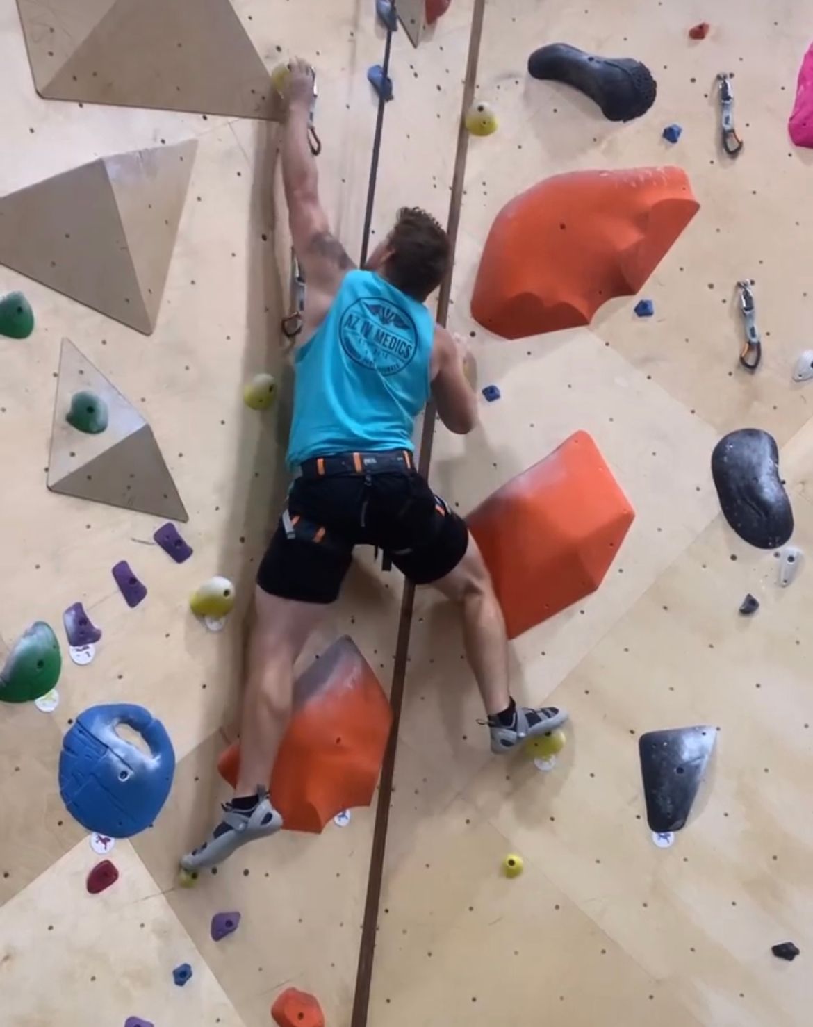 A man in a blue tank top is climbing a climbing wall
