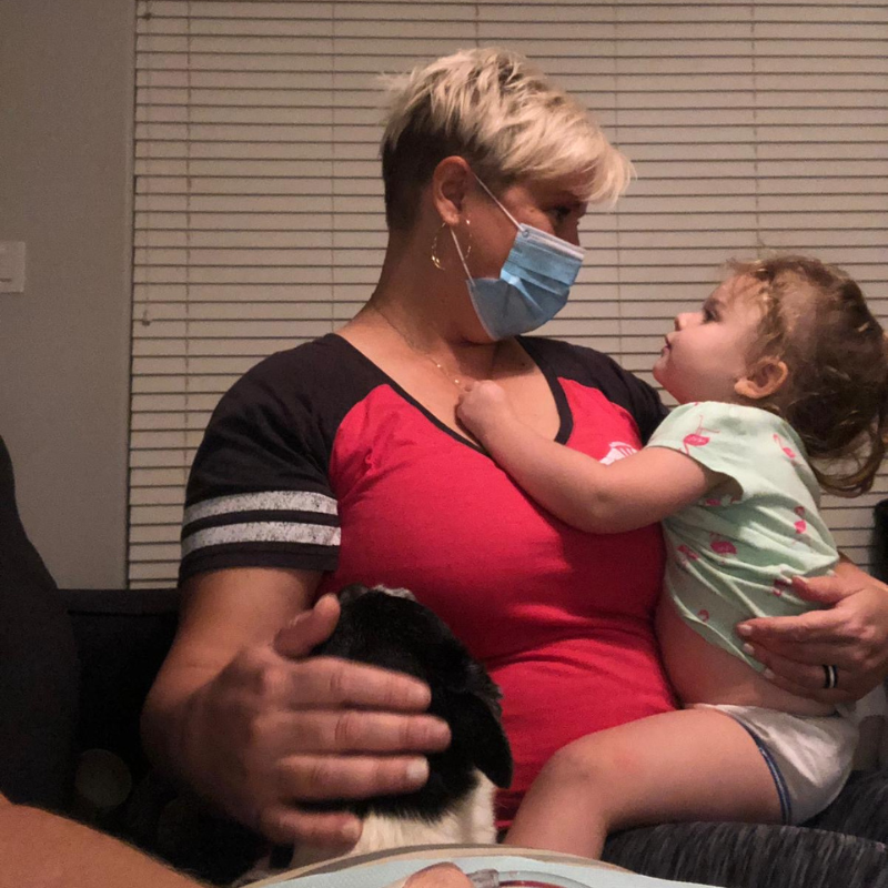 A woman wearing a mask is holding a little girl