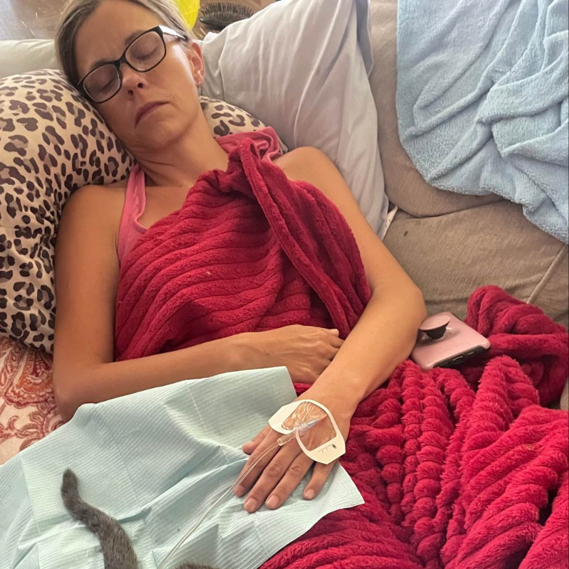 A woman is sleeping on a couch with a red blanket