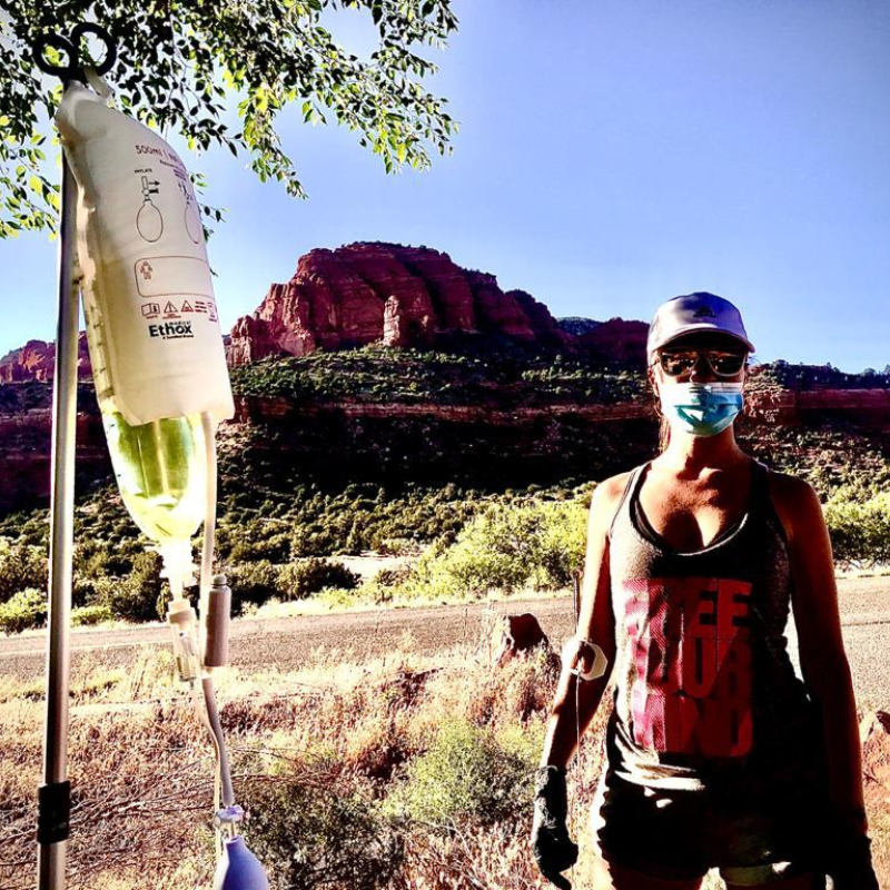 A woman wearing a face mask stands in front of a mountain