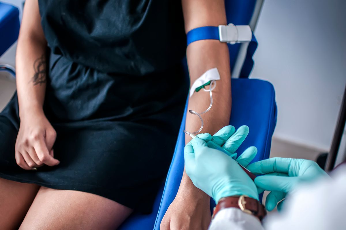 A medical professional in blue gloves prepares to draw blood from a patient's arm, which has a blue tourniquet applied.
