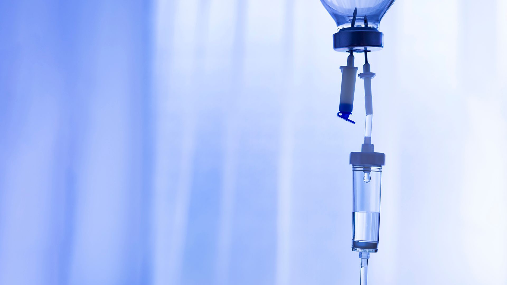 IV drip bag and tubing hanging against a blue hospital curtain