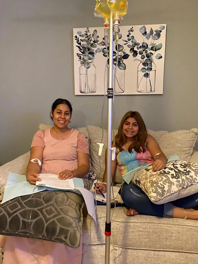 Two men are sitting on a bench with iv bags in their legs.