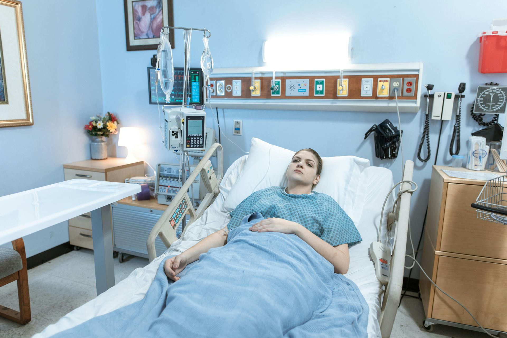 Woman in hospital bed with IV, pale blue walls, and medical equipment.