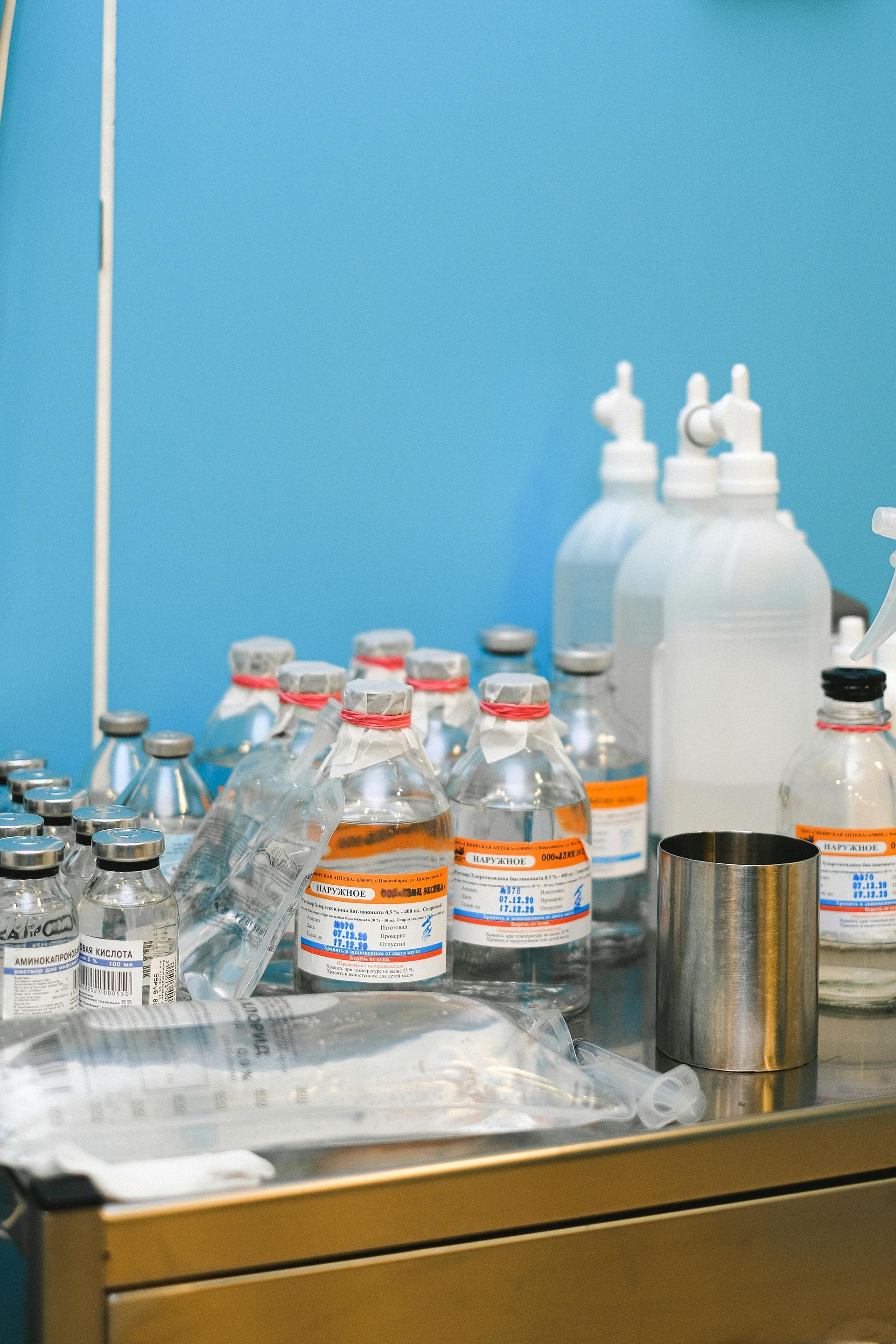 Medical bottles and containers on a stainless steel table, blue wall in background.