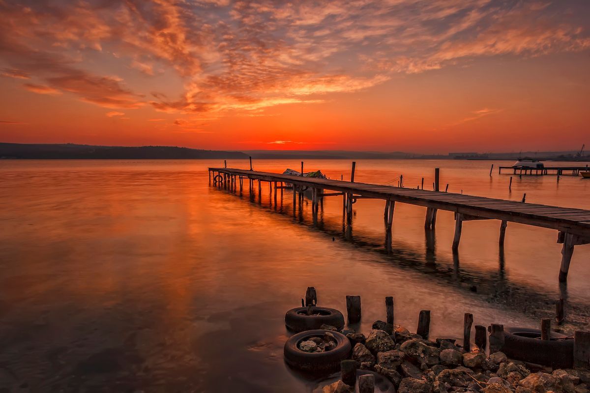 There is a dock in southern md in the middle of the water at sunset.