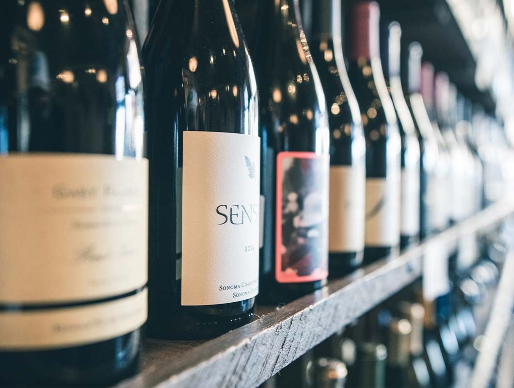A row of wine bottles are lined up on a wooden shelf.