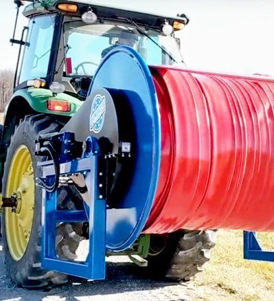 Tractor with blue hose reel winding a large red hose in a field