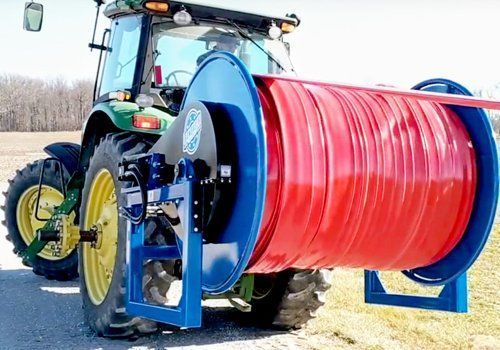 Tractor with a large red hose reel in a field, used for irrigation or spraying