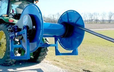 Blue agricultural machine attachment with large reels mounted on a tractor in a grassy field