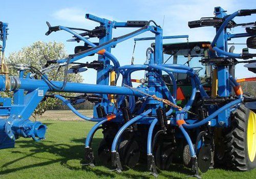Blue agricultural tillage machine with curved tines and yellow wheels in a field