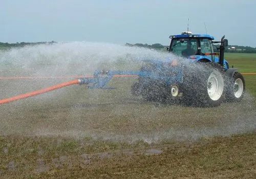 Tractor spraying water across a field, creating a wide mist