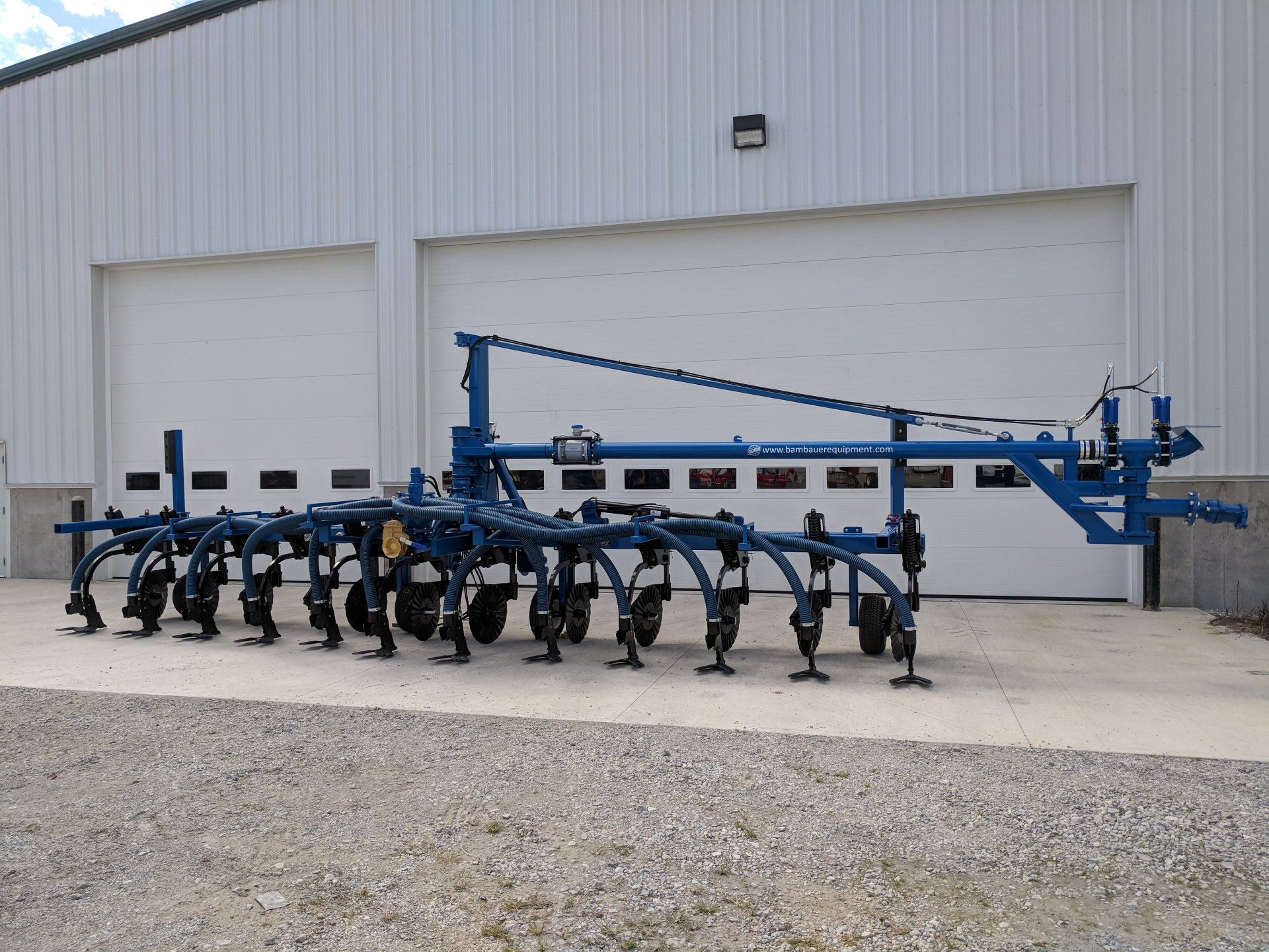Blue agricultural tillage implement parked outside a metal building on gravel.