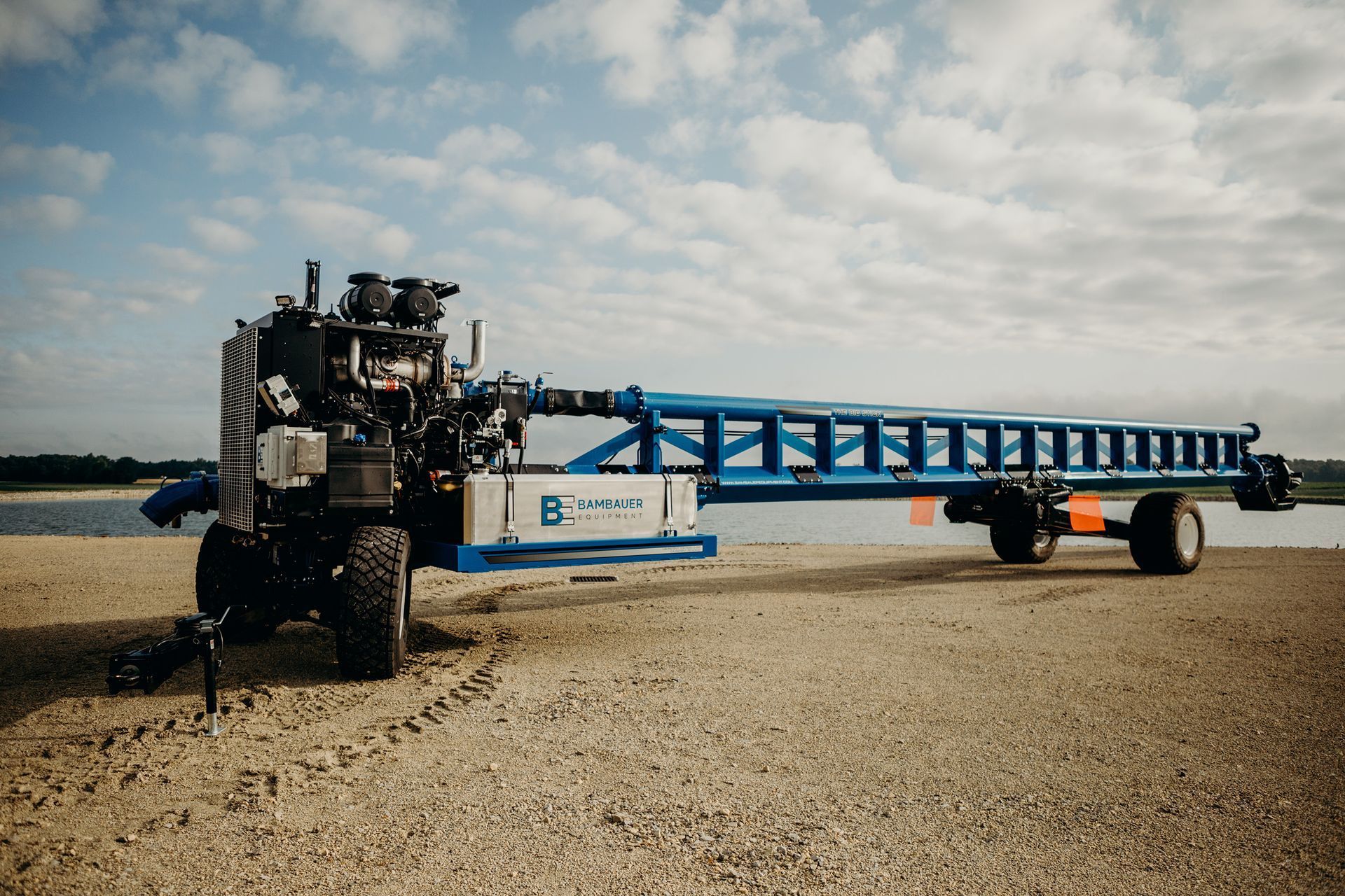 Blue farm equipment trailer on a gravel lot under a cloudy sky