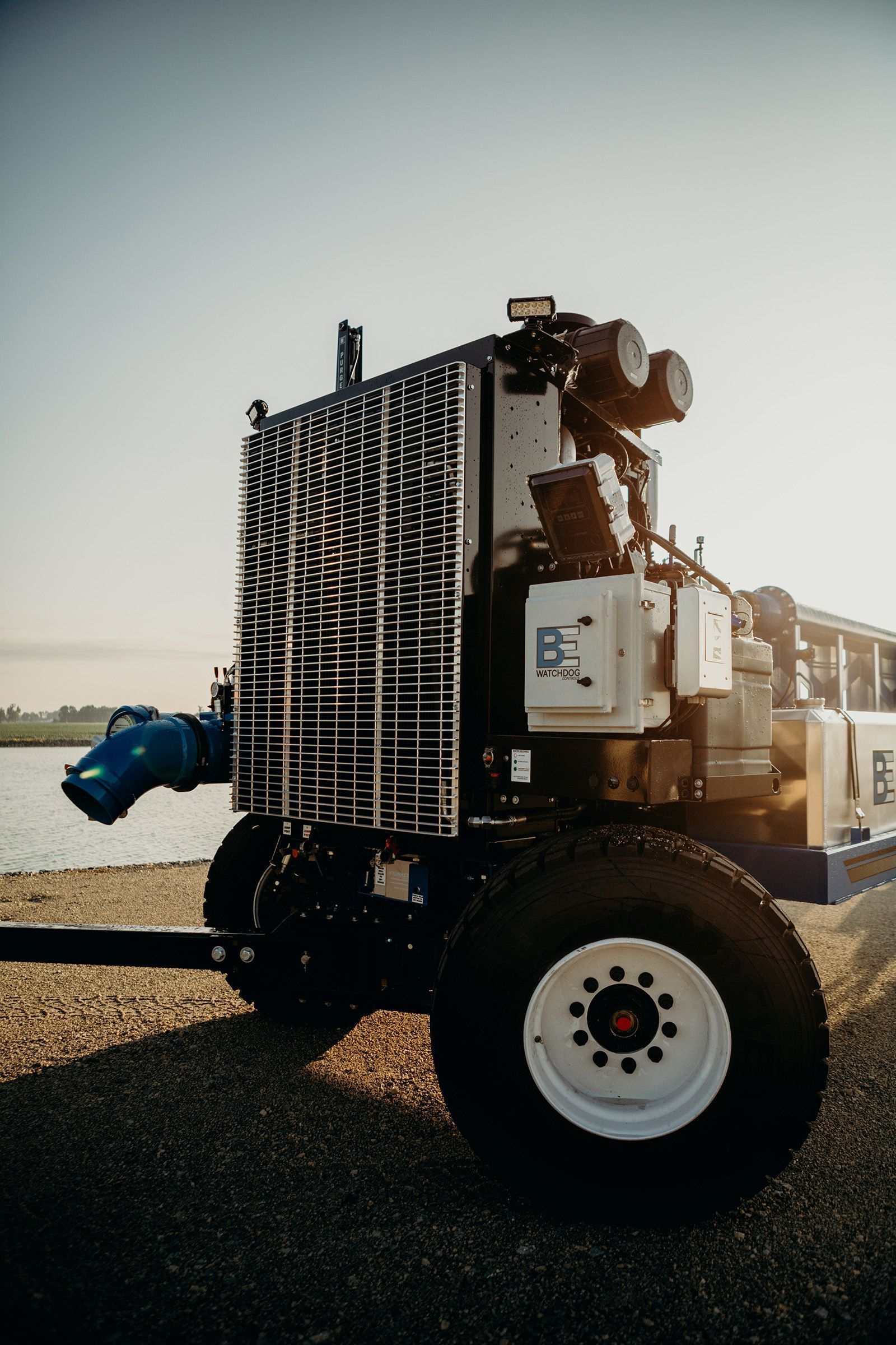 White industrial truck parked near water at sunset, with equipment mounted on the back.