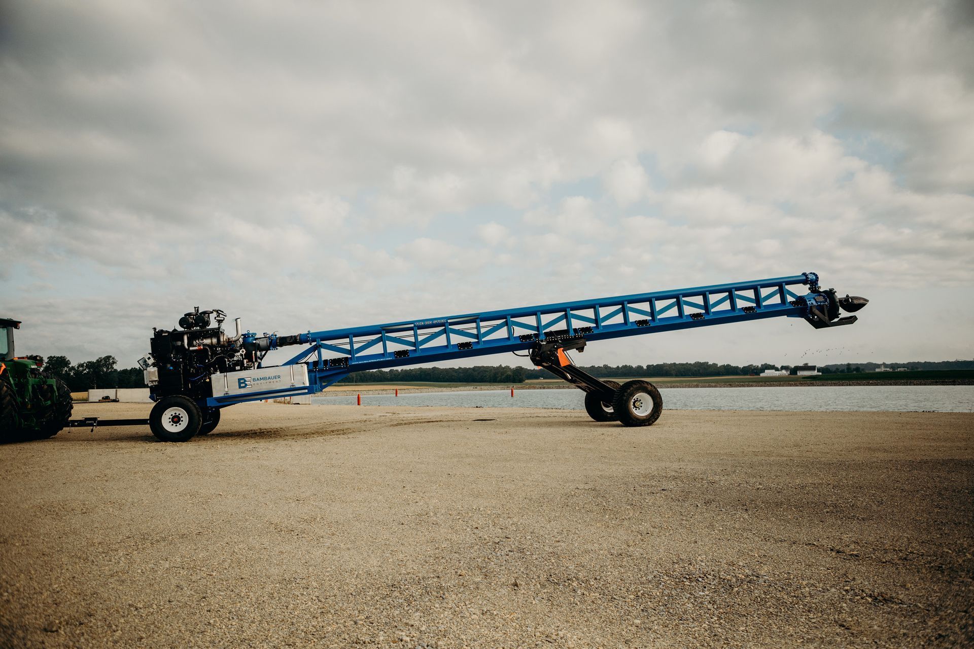 Blue agricultural sprayer boom cart on a gravel field under a cloudy sky