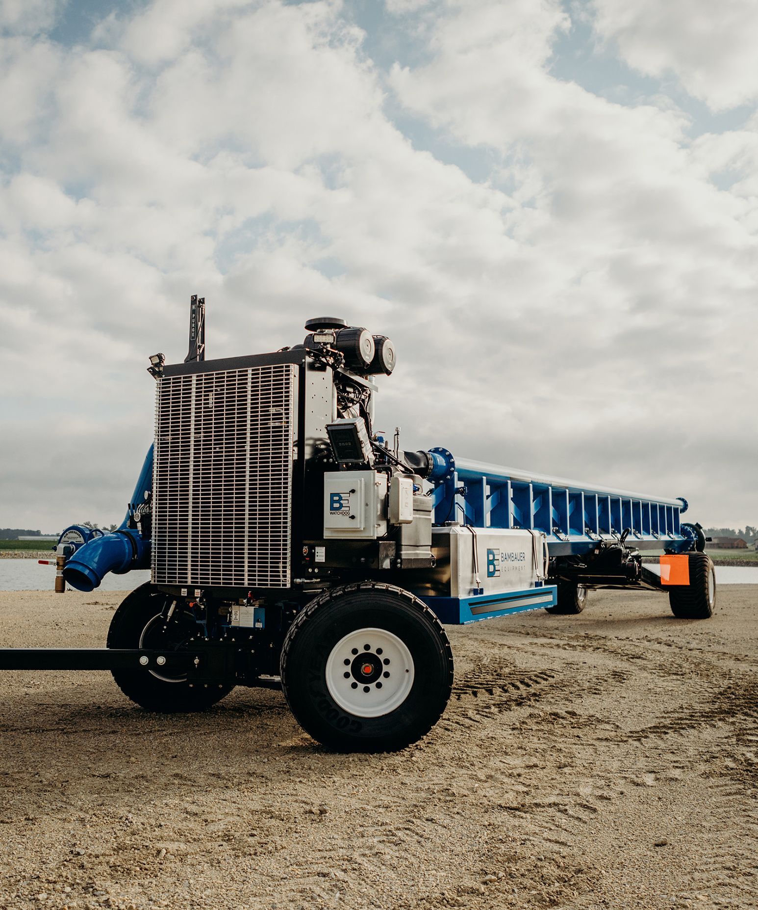Blue and white agricultural machine on gravel under a cloudy sky
