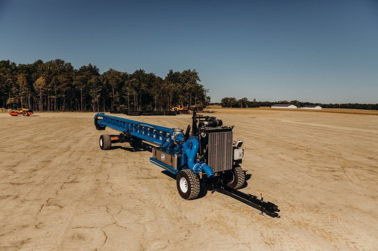 Blue agricultural conveyor machine on a sandy field under a clear sky