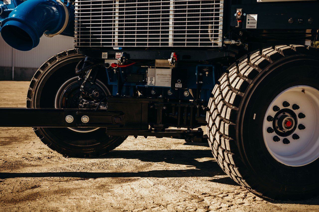 Close-up of a tractor’s front wheels and blue engine on a dirt surface