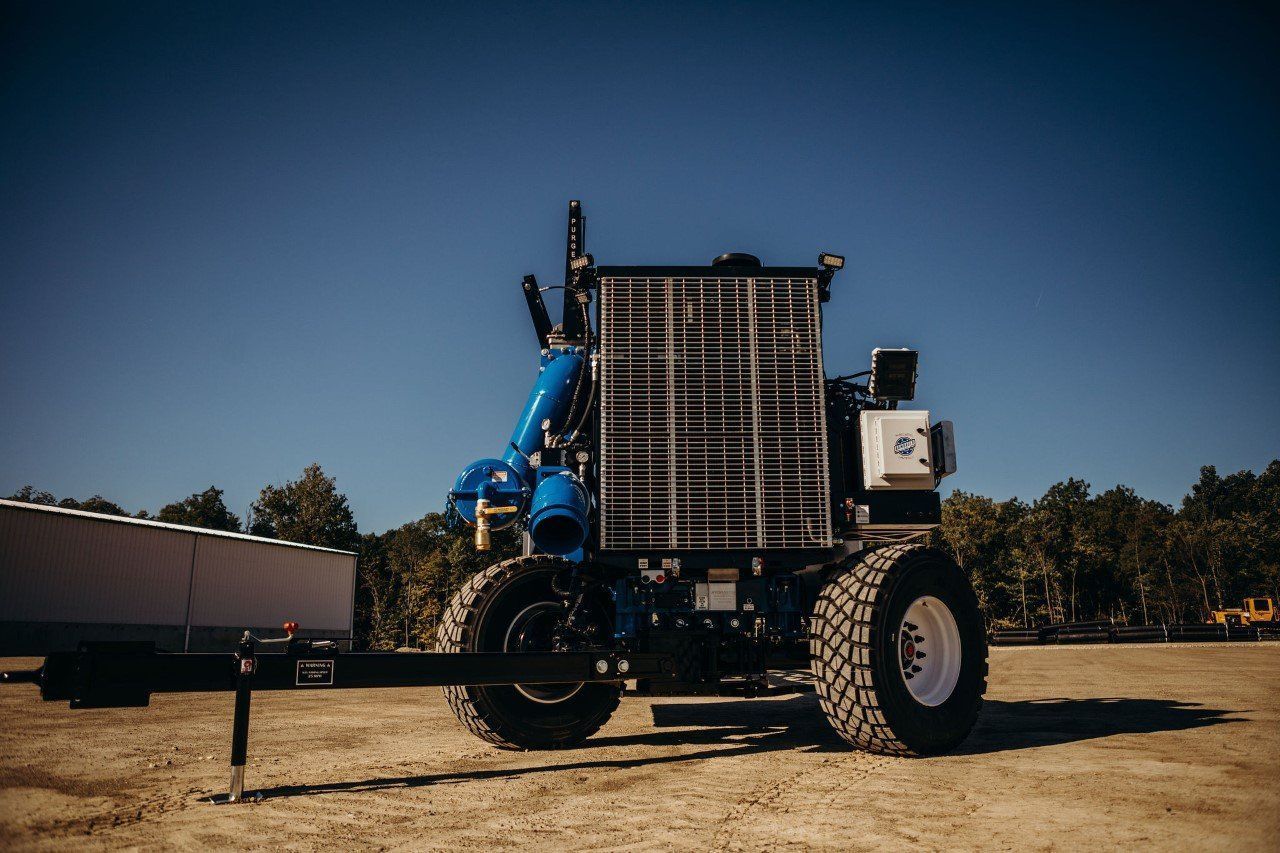 Blue off-road truck with oversized tires parked on a dirt lot under a clear sky