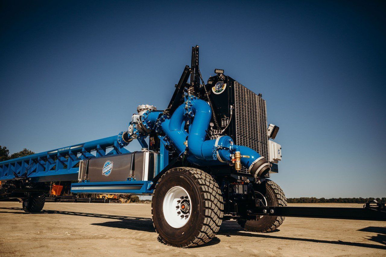 Blue agricultural machine with large tires and conveyor arm in a field under a clear sky