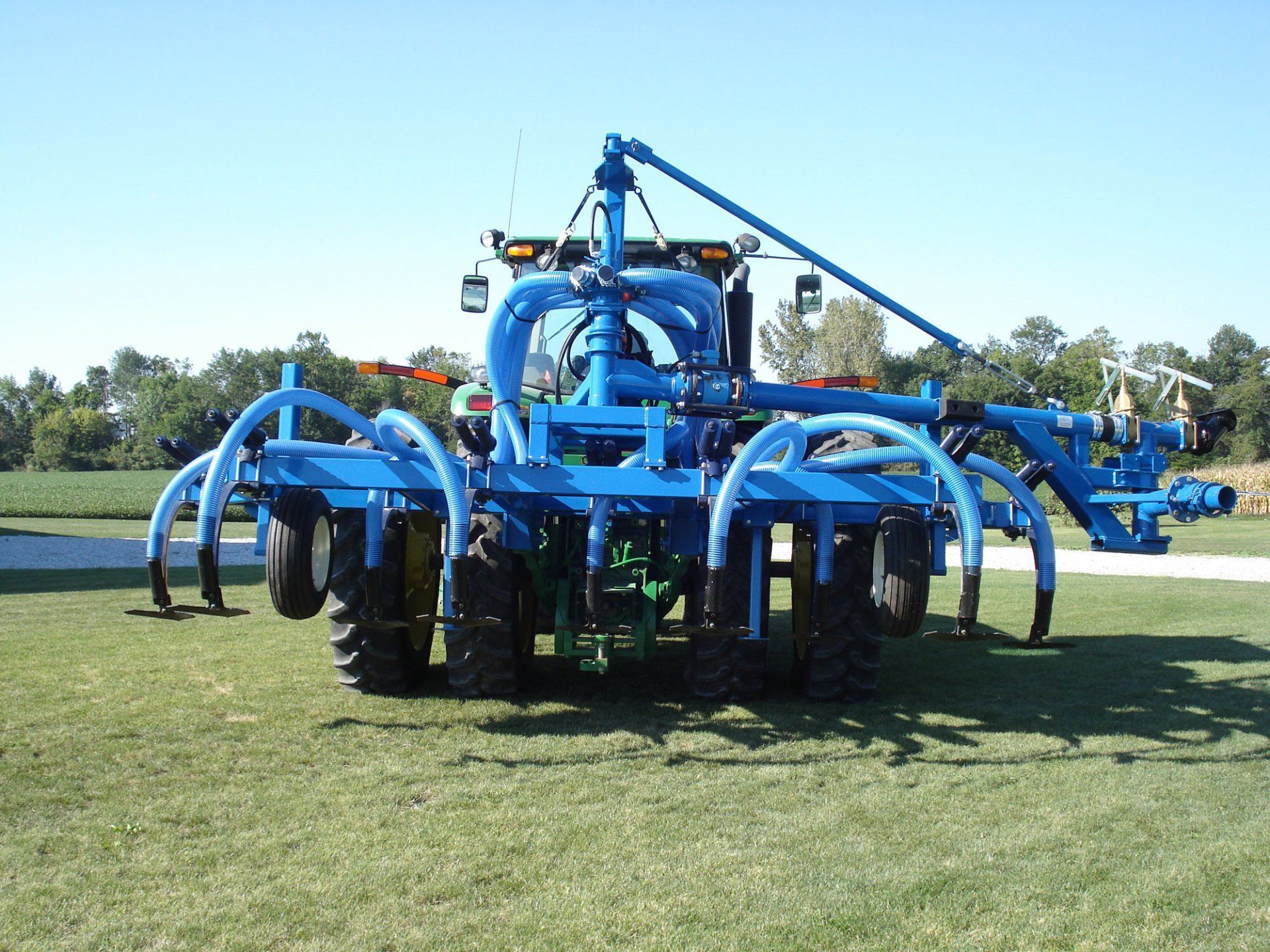 Blue farm machinery with curved arms parked on grass in a field under a clear sky