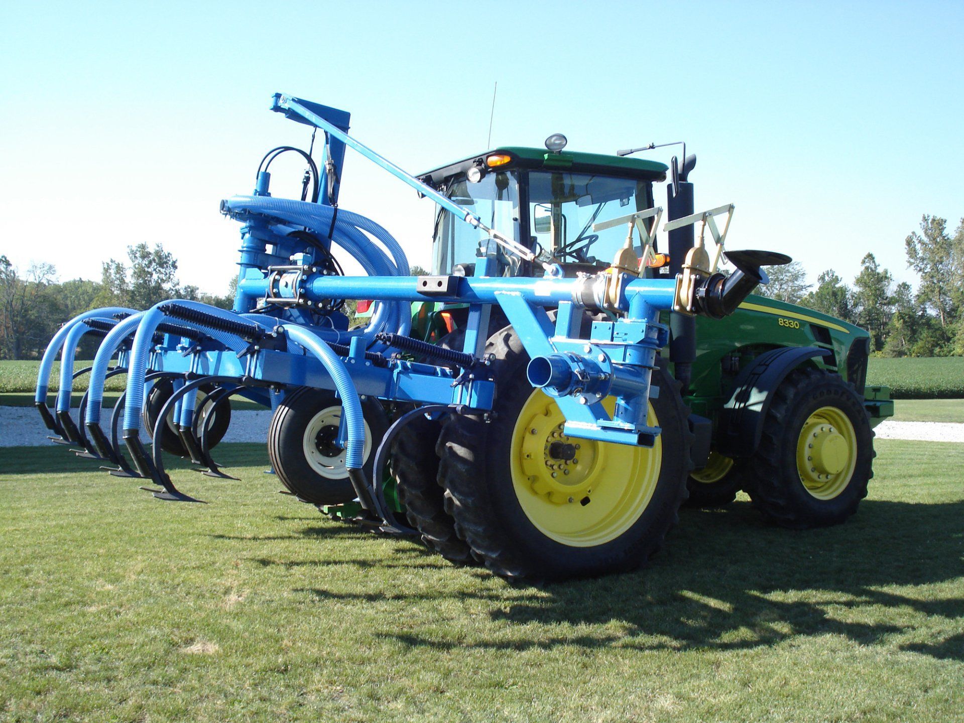 Blue agricultural tractor with large tillage implement parked on grass under a clear sky