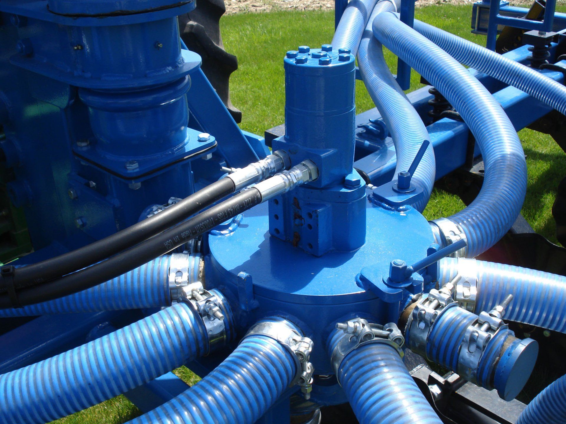Blue industrial pump assembly with multiple hoses and metal fittings connected around a central valve block