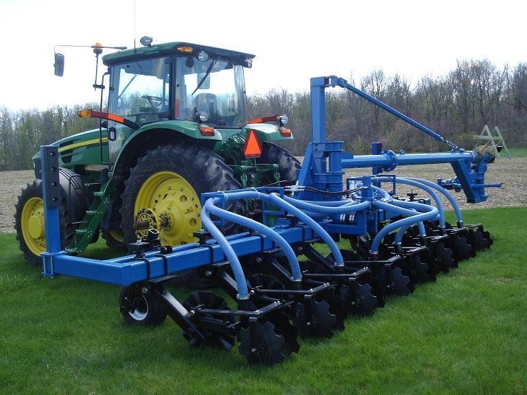 Tractor towing a blue agricultural cultivator across a grassy field