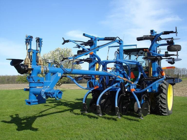 Blue agricultural tillage machine in a grassy field under a clear sky