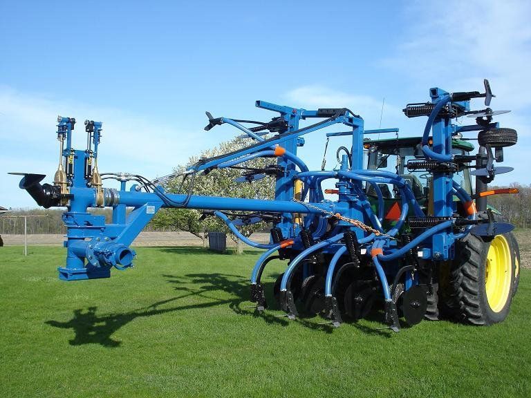 Blue farm sprayer attachment on a tractor in a grassy field
