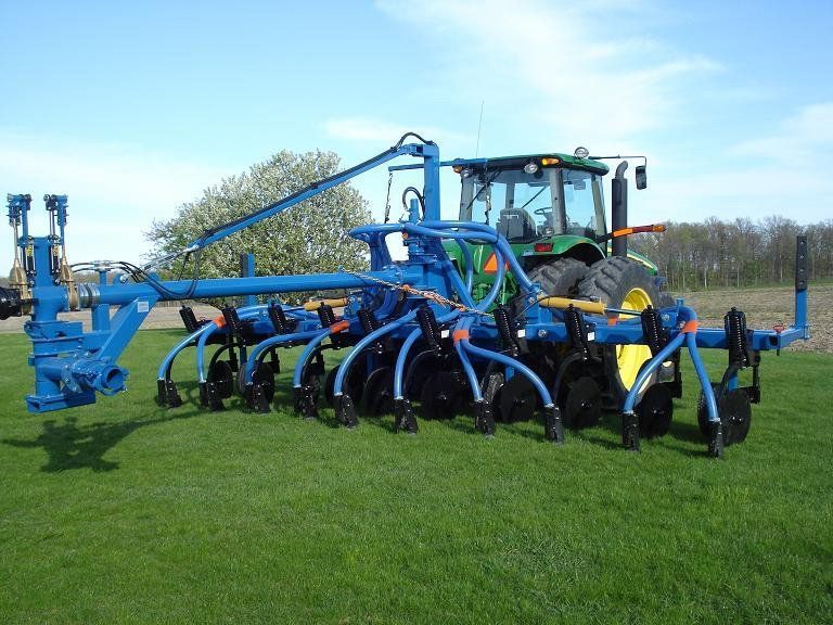 Blue farm implement attached to a tractor in a grassy field under a clear sky