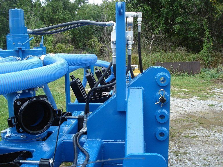 Blue industrial machinery with hoses and metal parts outdoors on gravel