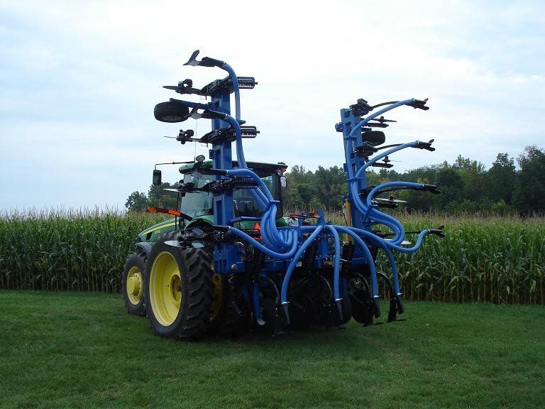 Blue farm tractor with large attached sprayer in a cornfield
