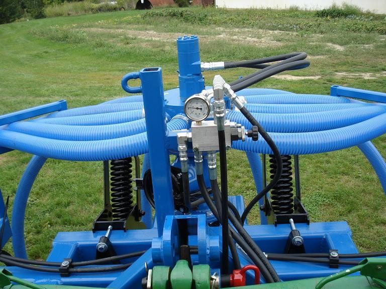 Blue farm machine with hoses and gauge on a grassy field