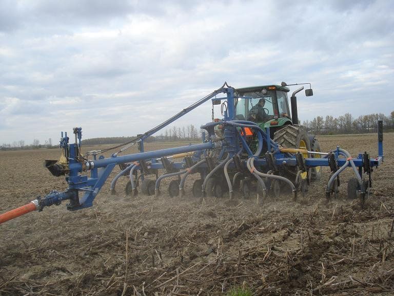 Blue tractor plowing a dry field under a cloudy sky