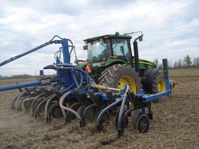 Green tractor with blue tillage equipment plowing a dusty field