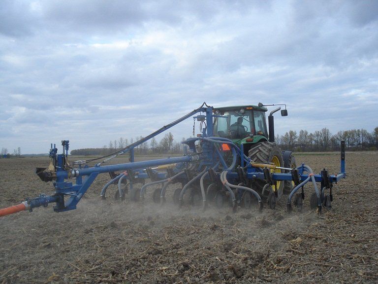 Blue farm sprayer spraying a field under a cloudy sky