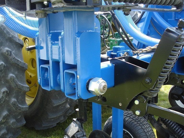 Close-up of blue agricultural machine parts with a black lever and tractor tire in the background