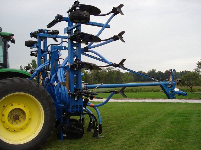 Blue agricultural machine mounted on a tractor in a grassy field