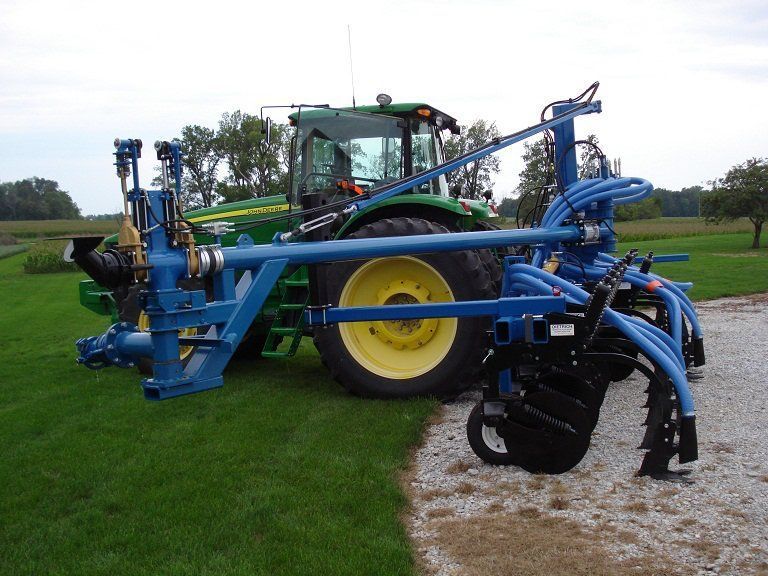 Blue farm machinery with large yellow wheel working beside a grassy field