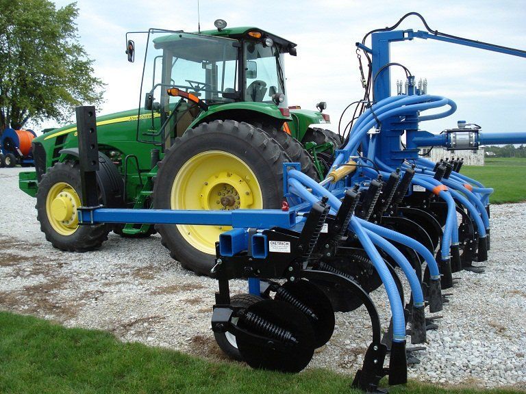 Green tractor towing a blue agricultural implement on a gravel field