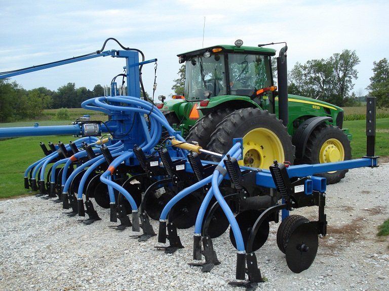 Blue agricultural planter attached to a green tractor in a gravel field