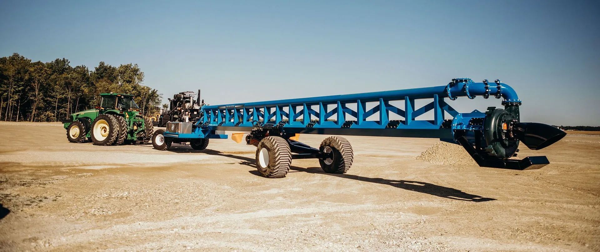 Blue farm irrigation boom being towed by a tractor across a dry field under a clear sky