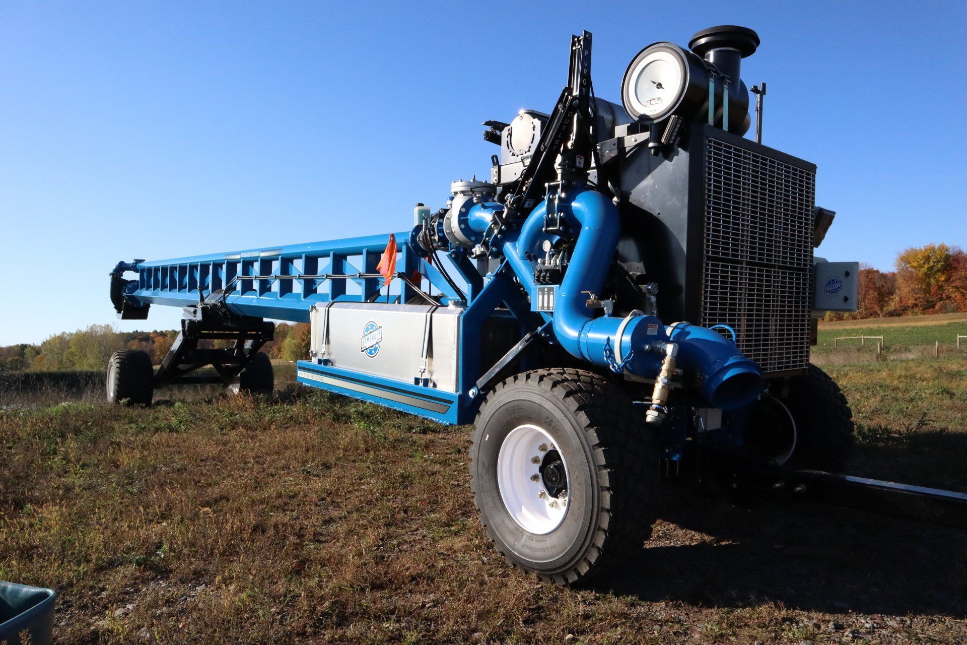 Blue agricultural sprayer tractor in a field, with large hose reels and pipes on a sunny day